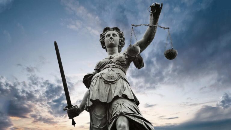 Majestic statue of Lady Justice holding scales and sword against a dramatic sky, symbolizing fairness and authority in the legal system.
